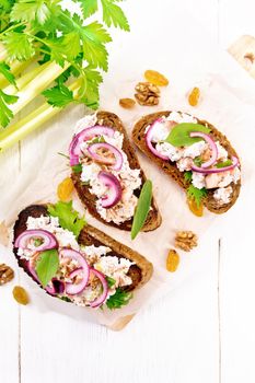 Salmon, petiole celery, raisins, walnuts, red onions and curd cheese salad on toasted bread with green lettuce on paper on a light wooden board background from above