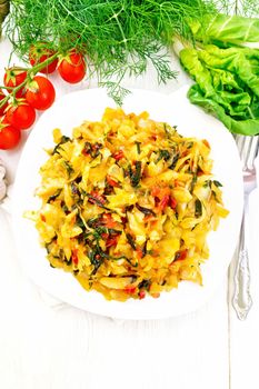 Cabbage stew with leaf beets and tomatoes in a white plate on napkin, parsley and a fork on the background of light wooden board on top