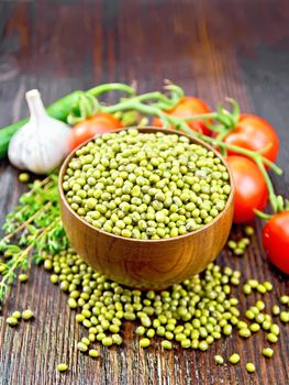 Green lentils mung in a bowl, hot pepper, garlic, thyme and red tomatoes on the background of dark boards