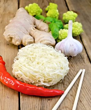 Stranded rice noodles with garlic, red pepper, ginger and basil, broccoli, chopsticks on a wooden boards background