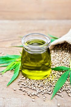 Hemp oil in a glass jar, grain in a bag and on the table, cannabis leaves on the background of an old wooden board