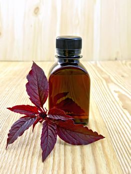 One vial of oil with leaves and flower maroon amaranth on a wooden boards background