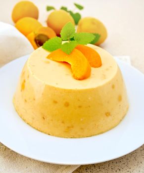 Dessert panna cotta cheesecake with apricots in a white plate, mint on a napkin, fruits on a background of brown granite table