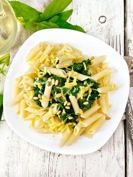 Penne pasta with spinach and cedar nuts in a plate on a napkin on a wooden board background on top