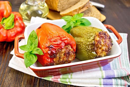 Two sweet peppers stuffed with meat and rice with basil leaves in a brown roasting pan on a napkin on a dark wooden boards background