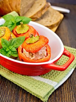 Three sweet peppers stuffed with meat and rice with basil leaves in red brazier on the green napkin, bread on a wooden boards background