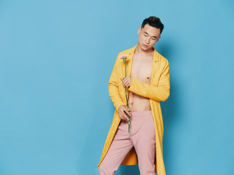 Fashionable man in a yellow coat with a flower in his hand on a blue background, Asian appearance. High quality photo