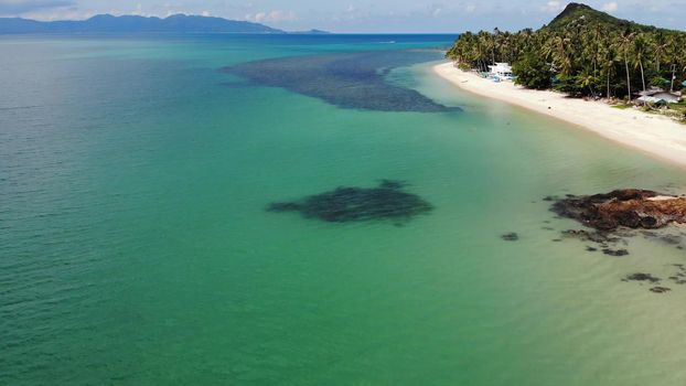 Green jungle and stony beach near sea. Tropical rainforest and rocks near calm blue sea on white sandy shore of Koh Samui paradise island, Thailand. Dream beach drone view. Relax and holiday concept