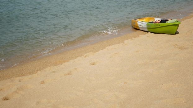 Kayak with paddles on sandy shore washed by waves of blue sea. Colorful canoe in wavy crystal water, tropical lonely island beach with copyspace. Outdoor activities, summer vacation, sport and health.