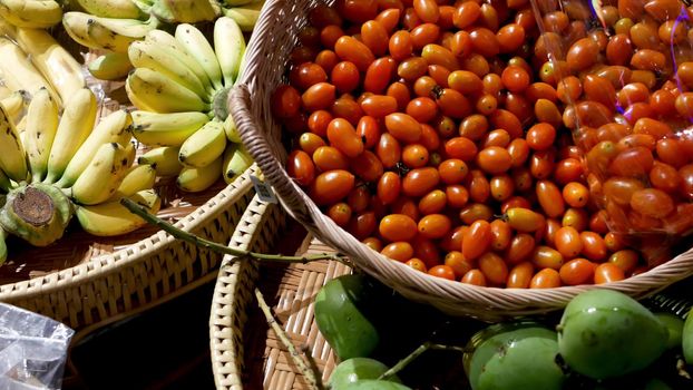 Fruits and vegetables on rustic stall. Assorted fresh ripe fruits and vegetables placed on rustic oriental stall in market. Green mango, tomatoes and yellow banana