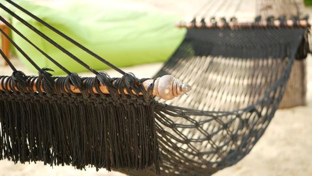 Black hammock stretching between coconut palms. Mesh vintage hipster hammock with fringe on edges stretched on sandy paradise beach of tropical island. Relax, travel vacation holiday resort concept