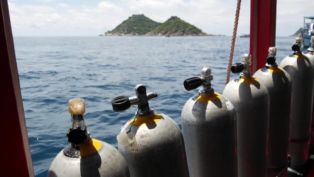 Row of oxygen tanks and diving equipment placed on modern boat in rippling ocean near Koh Tao resort, Thailand. Concept of tourist sports extreme entertainment, adventure and new experience