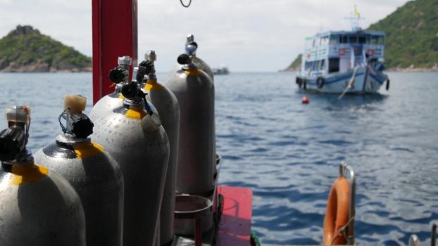 Row of oxygen tanks and diving equipment placed on modern boat in rippling ocean near Koh Tao resort, Thailand. Concept of tourist sports extreme entertainment, adventure and new experience