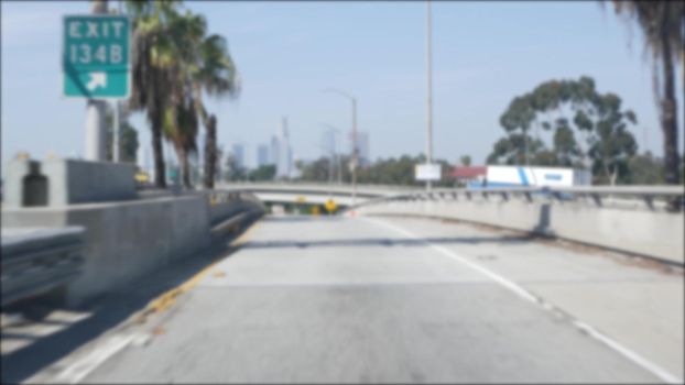 Driving on intercity freeway in Los Angeles, California USA. Defocused view from car thru glass windshield on busy interstate highway. Blurred suburb multiple lane driveway. Camera inside auto in LA.