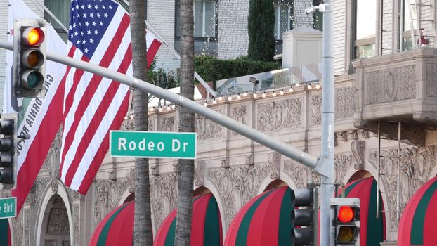 World famous Rodeo Drive Street Road Sign in Beverly Hills against American Unated States flag. Los Angeles, California, USA. Rich wealthy life consumerism, Luxury brands, high-class stores concept