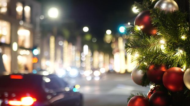 Closeup of Festively Decorated Outdoor Christmas tree with bright red balls on blurred sparkling fairy background. Defocused garland lights, Bokeh effect. Defocused night city street, cars on road.