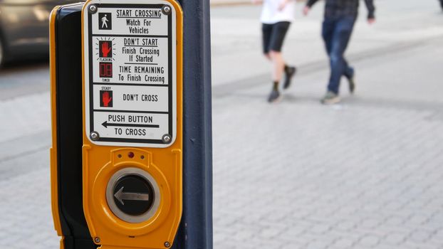 Traffic light button on pedestrian crosswalk, people have to push and wait. Traffic rules and regulations for public safety in USA. Zebra street crossing on road intesection in San Diego, California.