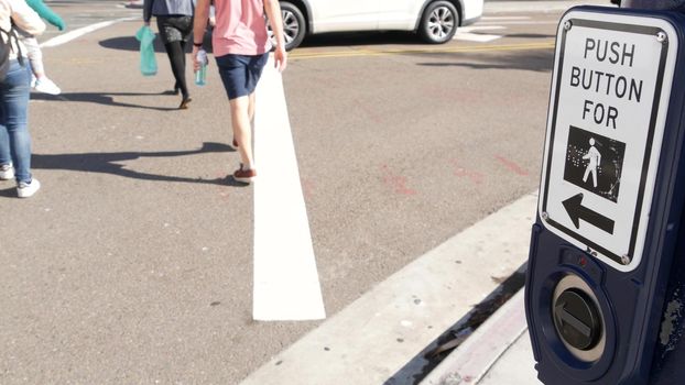Traffic light button on pedestrian crosswalk, people have to push and wait. Traffic rules and regulations for public safety in USA. Zebra street crossing on road intesection in San Diego, California.