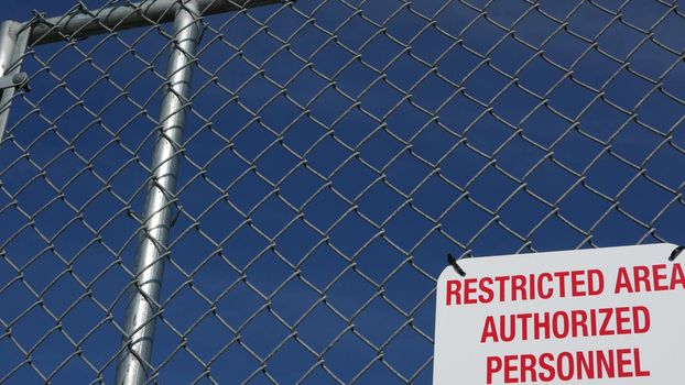 Restricted area, authorized personnel only sign in USA. Red letters, keep off warning on metal fence, United States border symbol. No trespassing notice means violators will be prosecuted by US law.