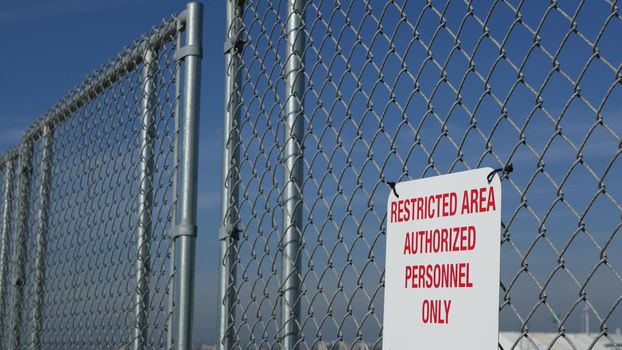 Restricted area, authorized personnel only sign in USA. Red letters, keep off warning on metal fence, United States border symbol. No trespassing notice means violators will be prosecuted by US law.