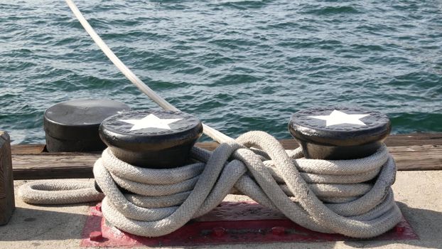 Tied rope knot on metallic bollard with stars, seafaring port of San Diego, California. Nautical ship moored in dock. Cable tie fixed on wharf. Symbol of navy marine sailing and naval fleet, USA flag.