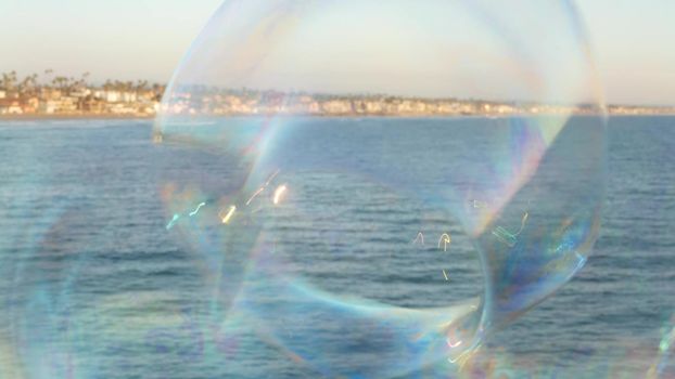 Blowing soap bubbles on ocean pier in California, blurred summertime background. Creative romantic metaphor, concept of dreaming happiness and magic. Abstract symbol of childhood, fantasy, freedom.