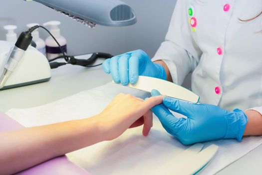 In a beauty salon, a woman is given a manicure using a nail file. Close-up.