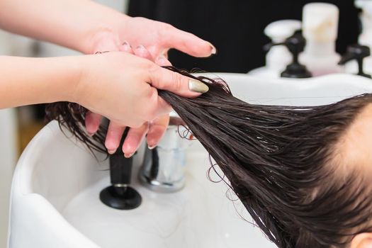 The hairdresser washes the head of a girl with long hair in the sink. Brown hair, close up