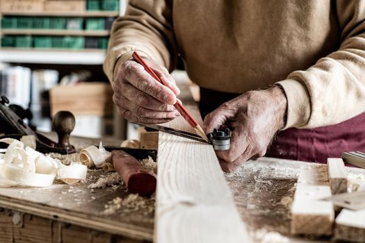 Carpenter making measurements with a pencil and a metal ruler on wooden plank