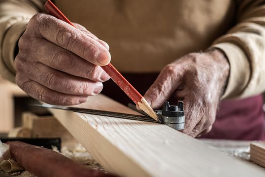 Carpenter measuring a plank with a red pencil and a metal ruler