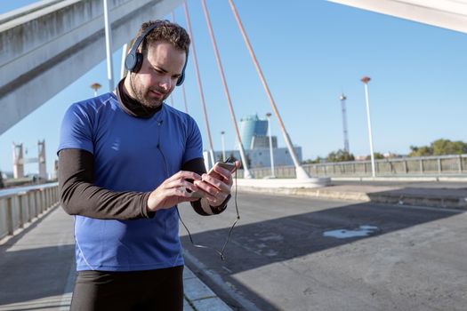 young man looking at his cell phone to listen to music while running through an urban area