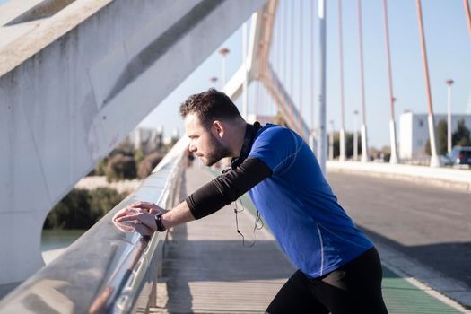 Closeup shot of a young male leaning on the border of the bridge while jogging