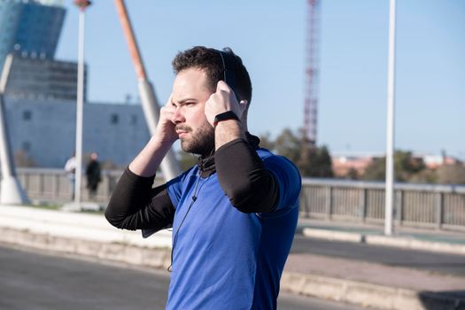 Closeup shot of a young male listening to music with headphones while jogging in the street