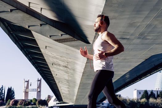 young man running in a white shirt across a bridge. He's listening to music and he's got some helmets on.