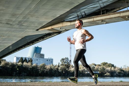 young man running in a white shirt across a bridge. He's listening to music and he's got some helmets on.