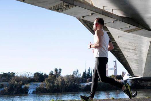 young man running in a white shirt across a bridge. He's listening to music and he's got some helmets on.