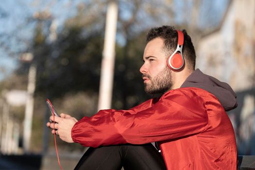 Closeup shot of a young male in red headphone listening to music while working out in the street