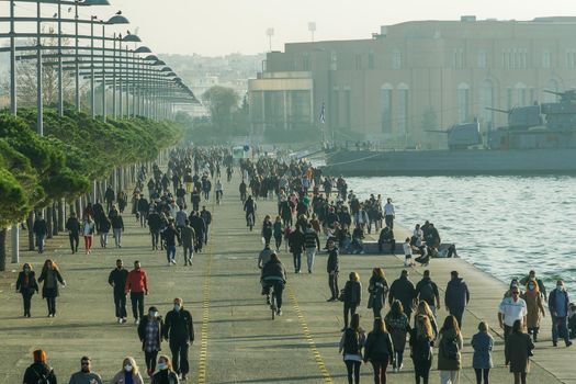 Unidentified persons with face protection walk at close distance on the pedestrian area of the city waterfront in Thessaloniki, Greece.