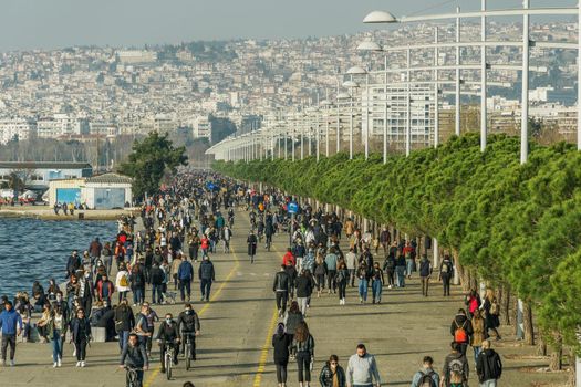 Unidentified persons with face protection walk at close distance on the pedestrian area of the city waterfront in Thessaloniki, Greece.