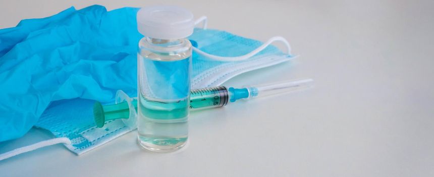 A syringe, gloves, mask, and a bottle of vaccine stand on a blue background. For the prevention, immunization and treatment of coronavirus infection. The concept of medicine and health care.