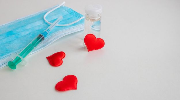 On a white background are a mask, a syringe, a bottle of vaccine and three small red hearts. The concept of medicine and health care.