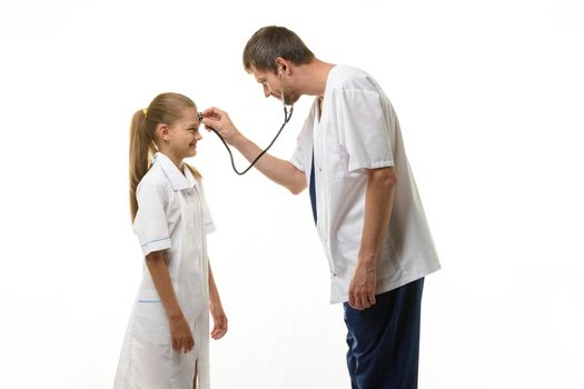 The doctor put the head of the phonendoscope to the forehead of the girl in a medical gown