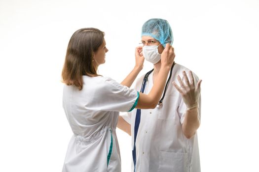 Nurse putting medical mask on surgeon face isolated on white