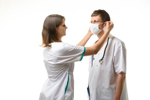 The nurse puts a medical mask on the doctor's face with glasses