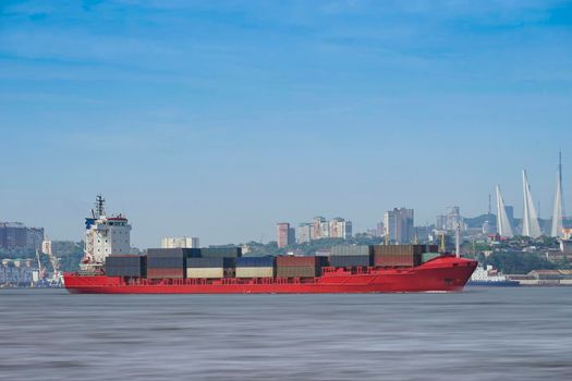 Seascape with a red container ship on the background of the cityscape. Vladivostok, Russia