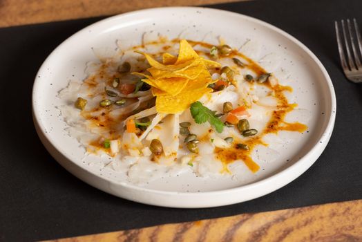 White plate with Cod Carpaccio with chili vinaigrette, pumpkin seeds and chips