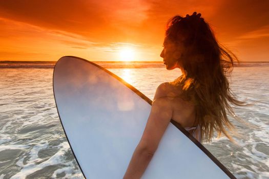 Beautiful woman on tropical beach holding surfboard at sunset in Bali