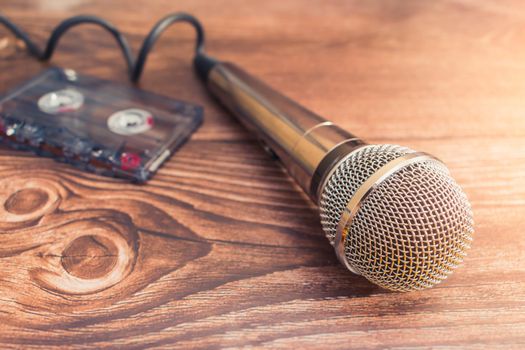 Silver microphone and old audio cassette with music lie on a wooden table in a recording studio