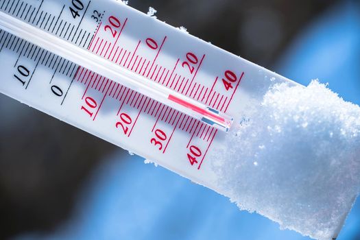 The thermometer lies on the snow in winter showing a negative temperature. Meteorological conditions in a harsh climate in winter with low air and ambient temperatures.Freeze in wintertime