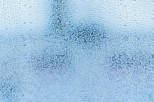 Wet glass with large drops of water or rain of blue color. Background or wallpaper with water texture close-up. Image of water droplets on a clear glass surface during heavy rain